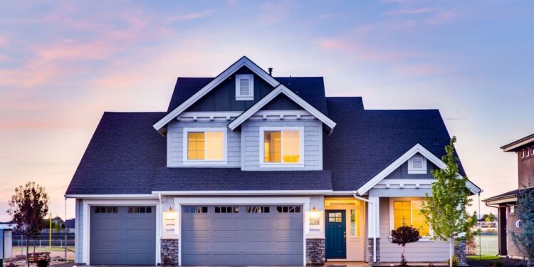 Modern two-storey grey suburban house with a three-car garage lit at twilight