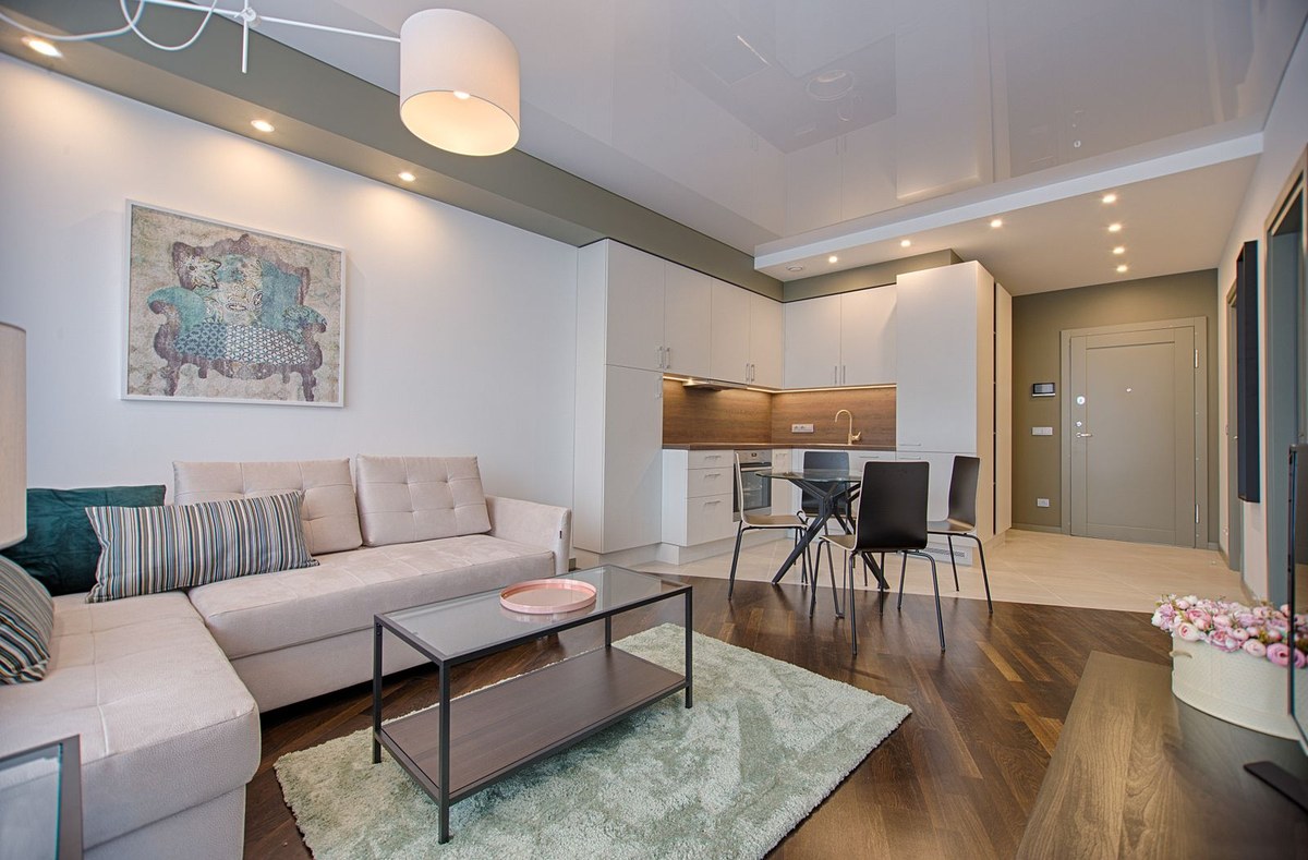 Staged modern apartment with beige sectional sofa, open kitchen, and glass dining table